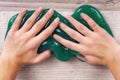 Young girlÃ¢â¬â¢s hands squeezing green slime on a wooden table